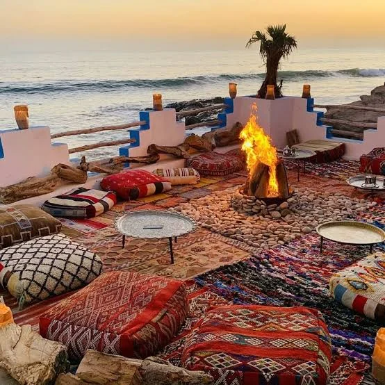 Beach lounge with patterned cushions and a bonfire by the ocean at sunset