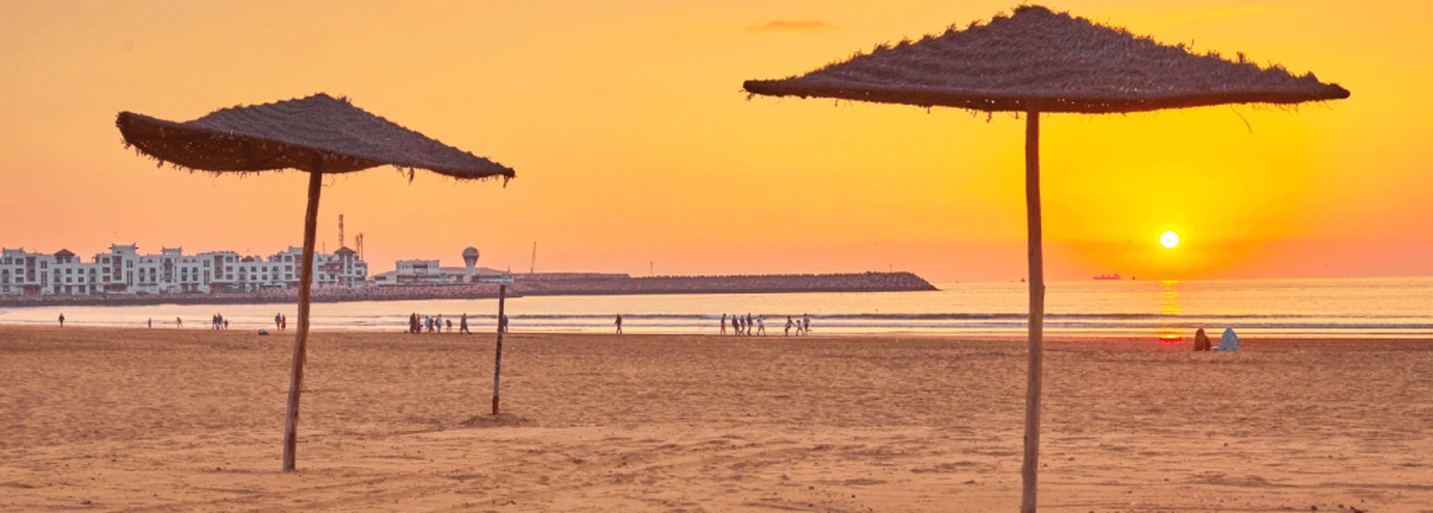 Agadir beach at golden sunset with straw umbrellas and ocean waves