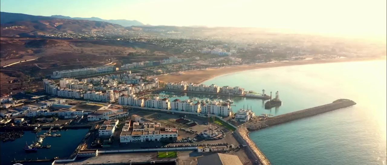 Aerial view of Agadir coastline at sunset — curved sandy bay, marina and white city along the Atlantic