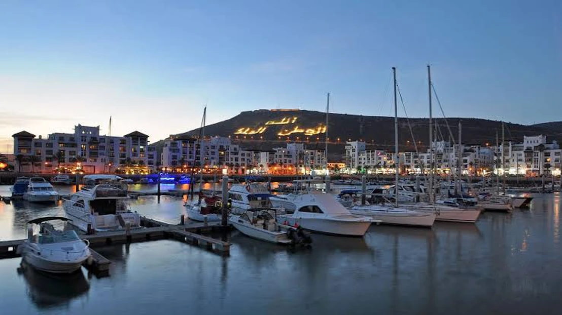 Agadir Marina harbor at twilight with yachts docked and illuminated Kasbah hill in the background