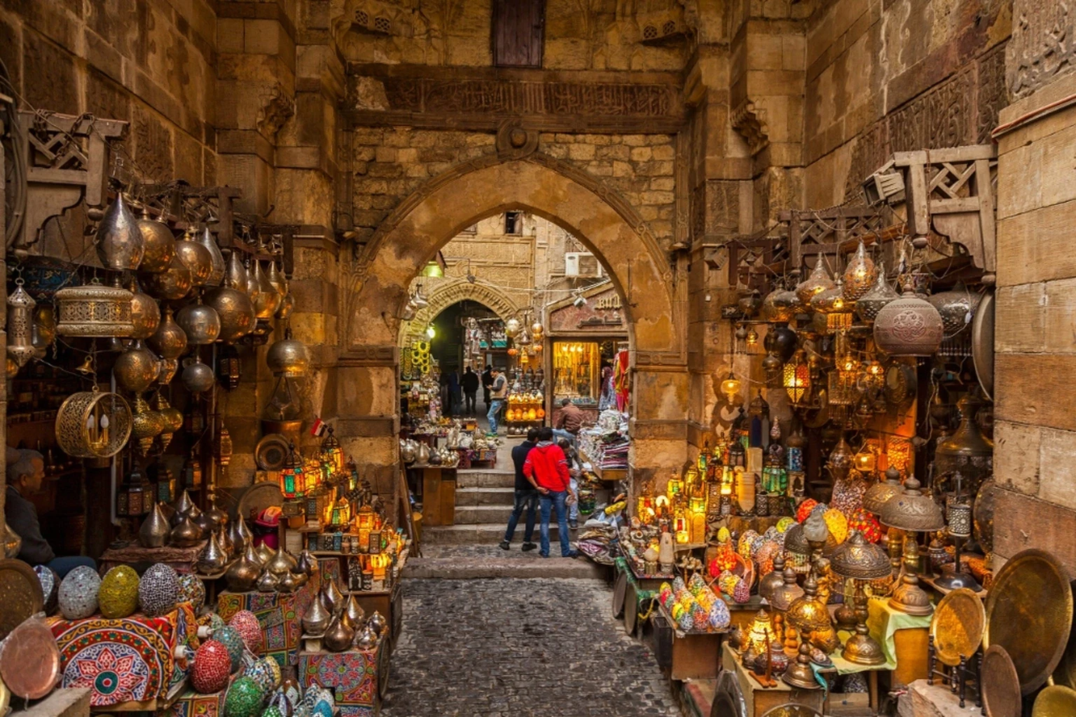 Souk El Had market alley with traditional glowing Moroccan lanterns, brass lamps and stone arches